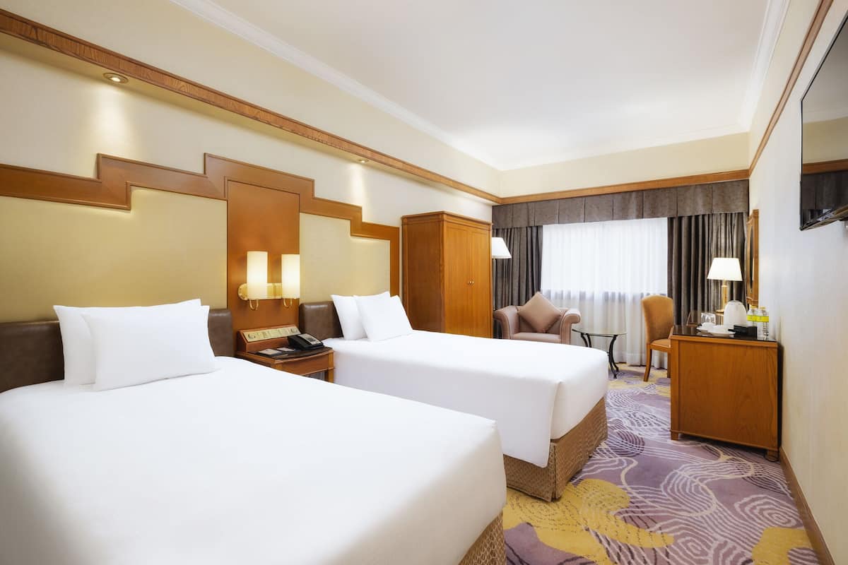 A hotel room with two beds, a desk, a chair, and a window with curtains.