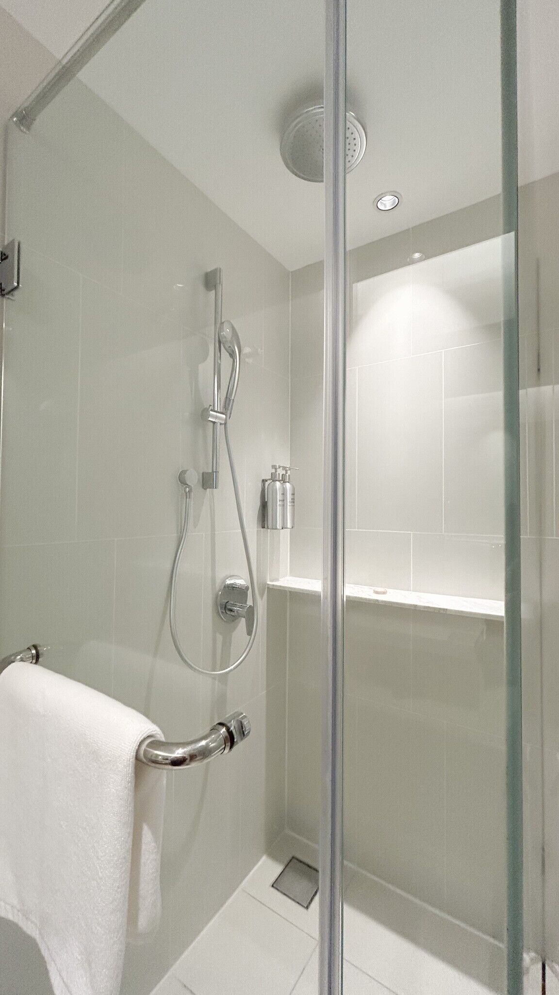 Ein moderner Duschbereich mit Glastür, Handbrause und am Wand montiertem Wasserhahn.