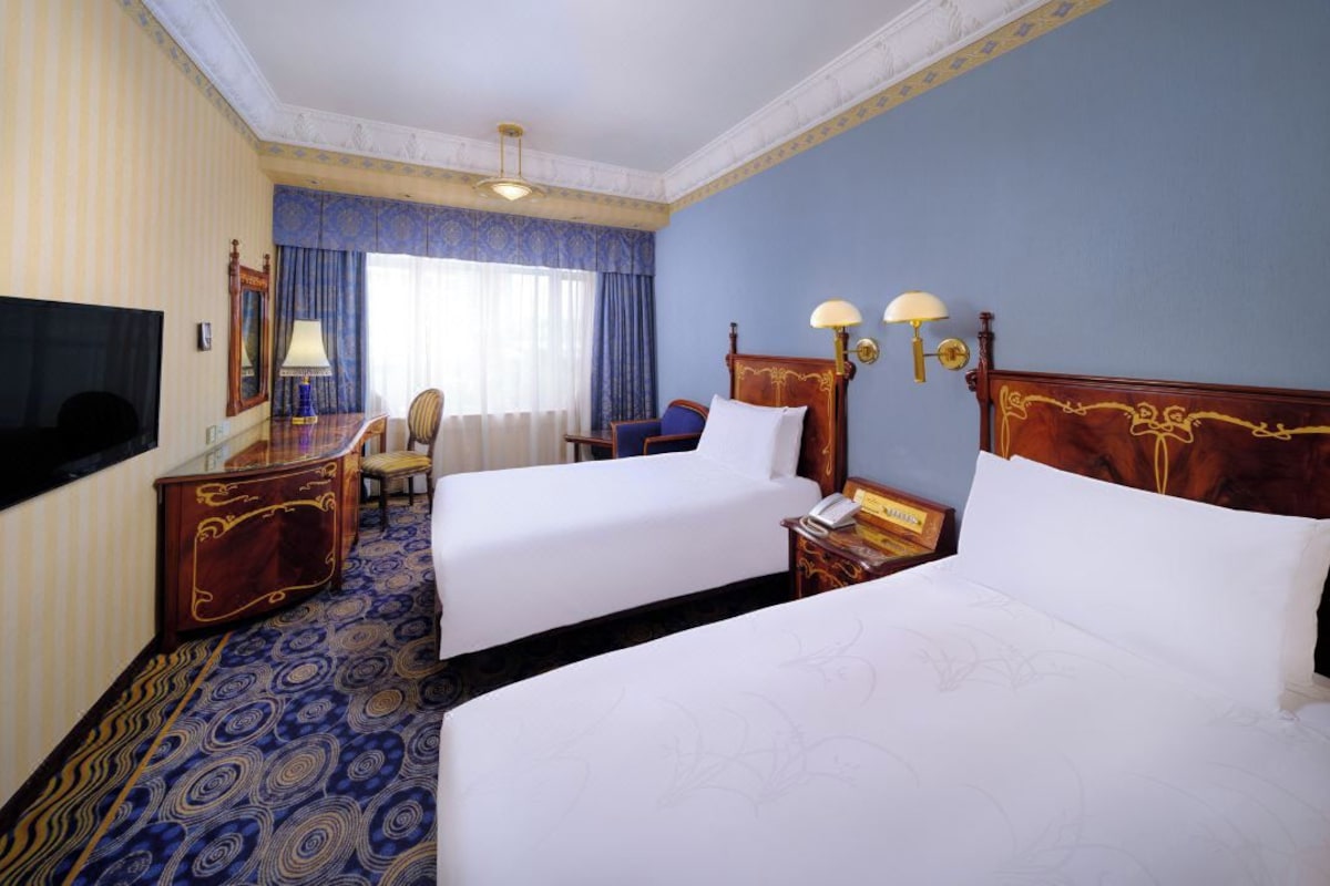 Una habitación de hotel con dos camas, un escritorio, una silla, un televisor y un teléfono.