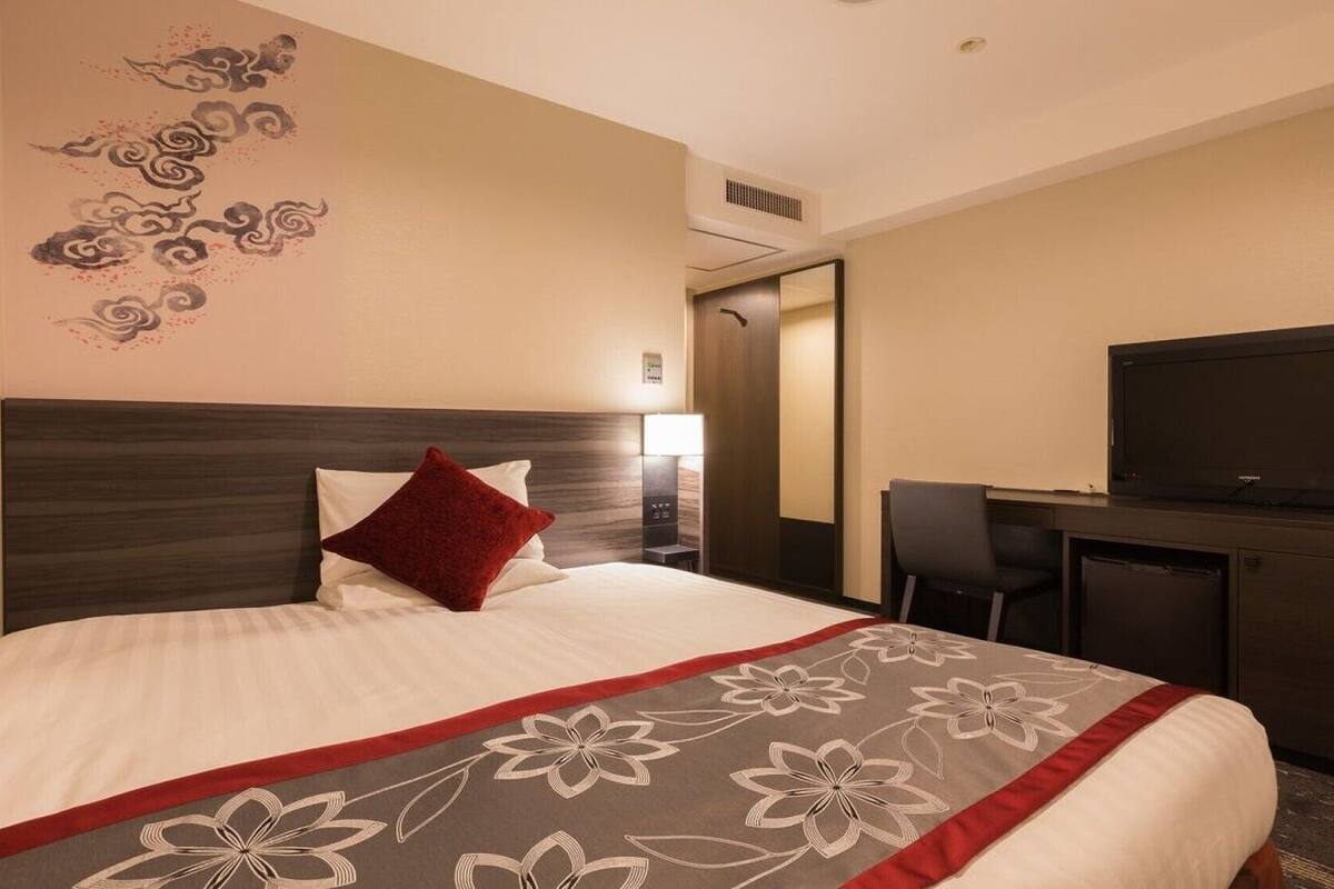 A hotel room with a bed, a TV, a desk, and a chair.