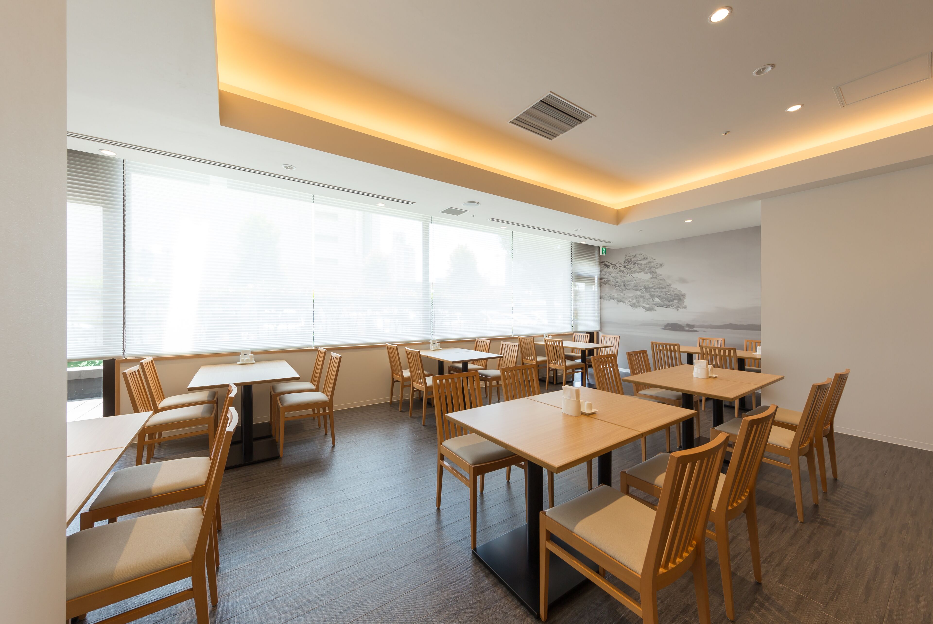 A spacious dining area with multiple tables and chairs, large windows, and a modern ceiling design.