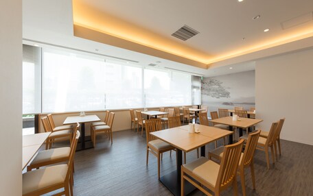 A spacious dining area with multiple tables and chairs, large windows, and a modern ceiling design.