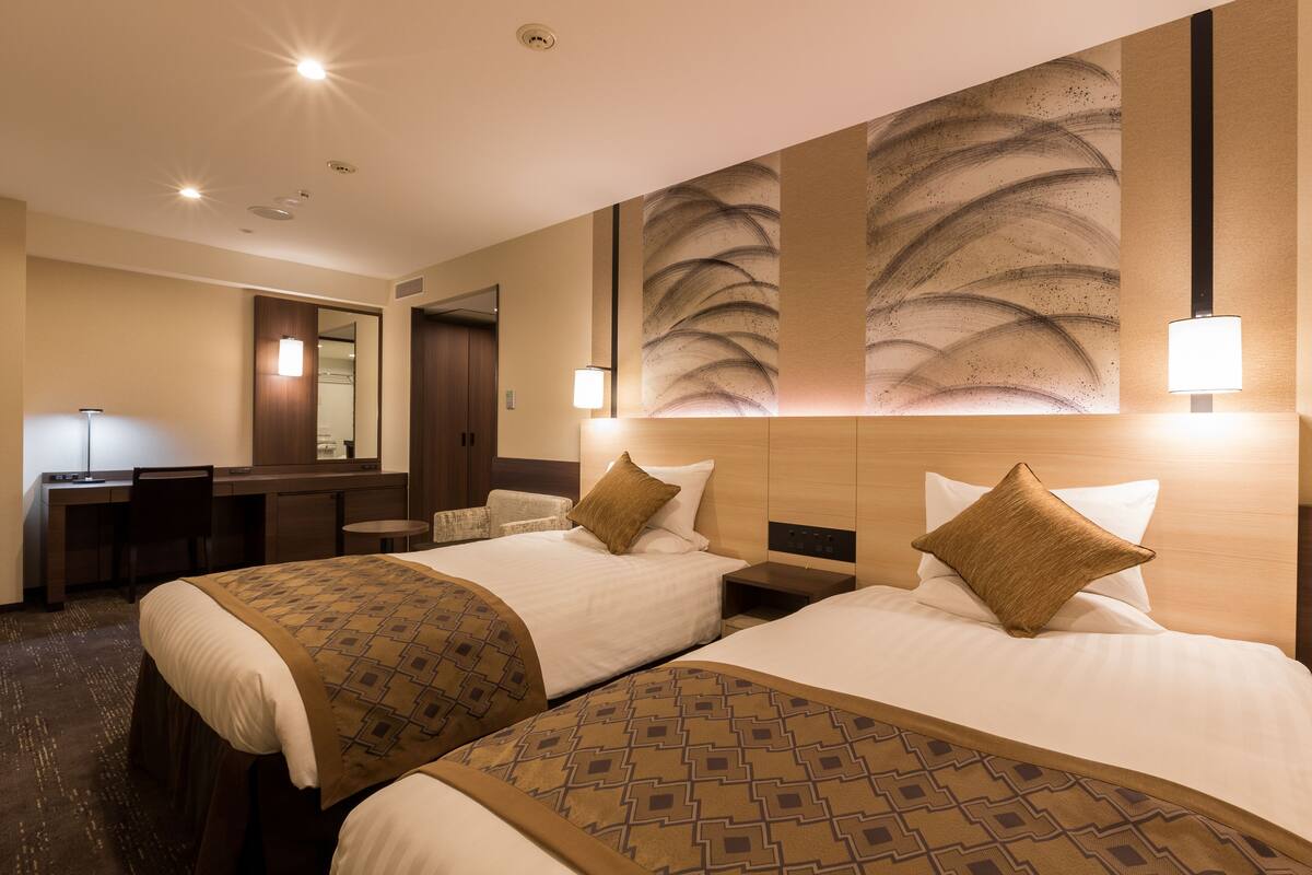 A hotel room with two beds, a desk, and a mirror.