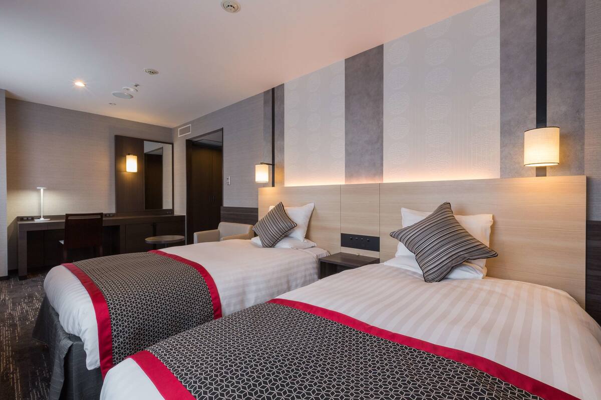 A hotel room with two beds, a desk, and a mirror.