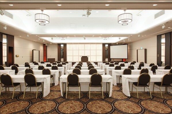 A conference room with rows of tables and chairs, a podium, and a projector screen.