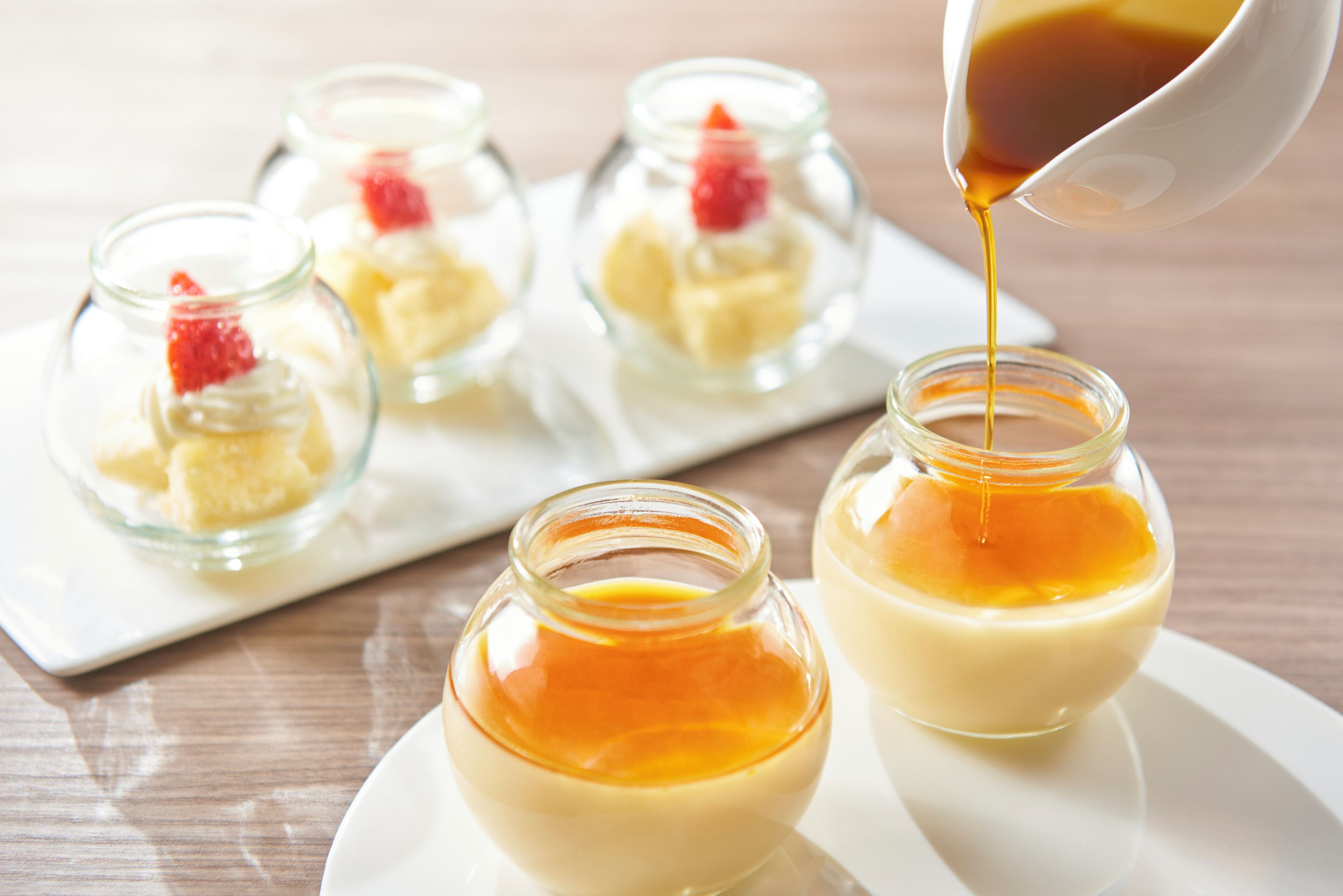 A dessert presentation with small glass jars containing creamy dessert topped with caramel and a strawberry.