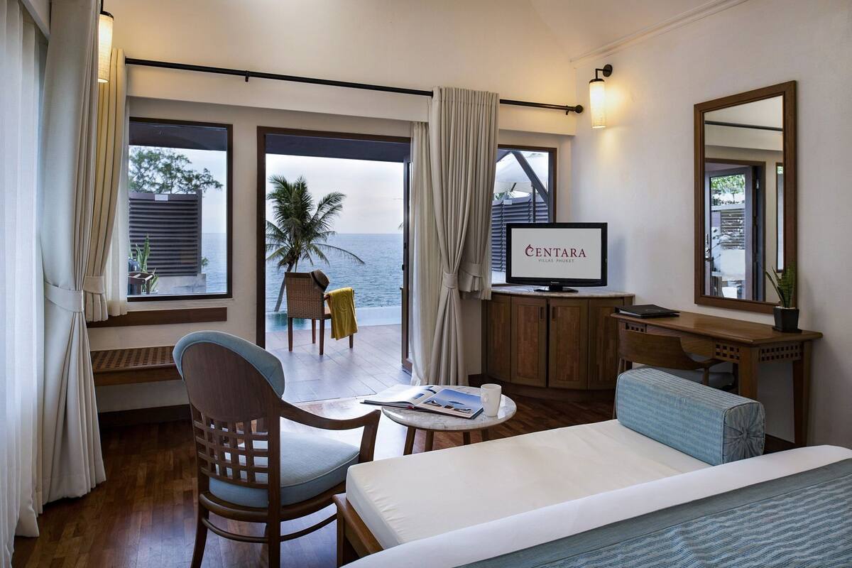 A hotel room with a bed, a desk, a chair, a TV, and a view of the ocean.