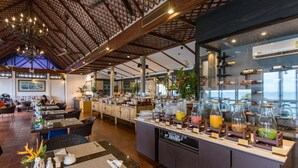 A restaurant with a high ceiling, a central bar area with a variety of drinks, and a seating area with tables and chairs. - Centara Villas Phuket (Karon)