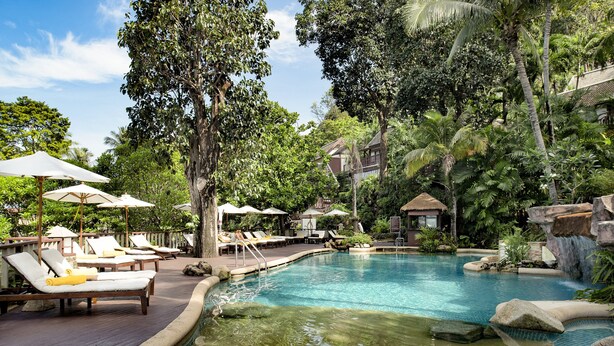 A pool area with lounge chairs and umbrellas, surrounded by lush greenery and a waterfall feature. - Centara Villas Phuket (Karon)