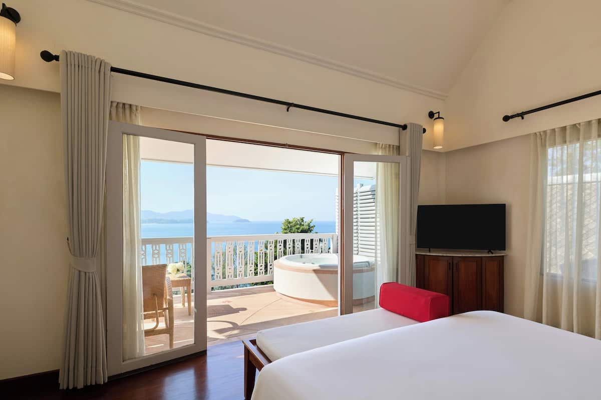 A hotel room with a bed, a TV, a balcony with a hot tub, and a view of the sea.