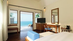 A hotel room with a bed, a desk with a chair, a television, a small table with a tray, and a large window offering a view of the ocean. - Centara Villas Phuket (Karon)
