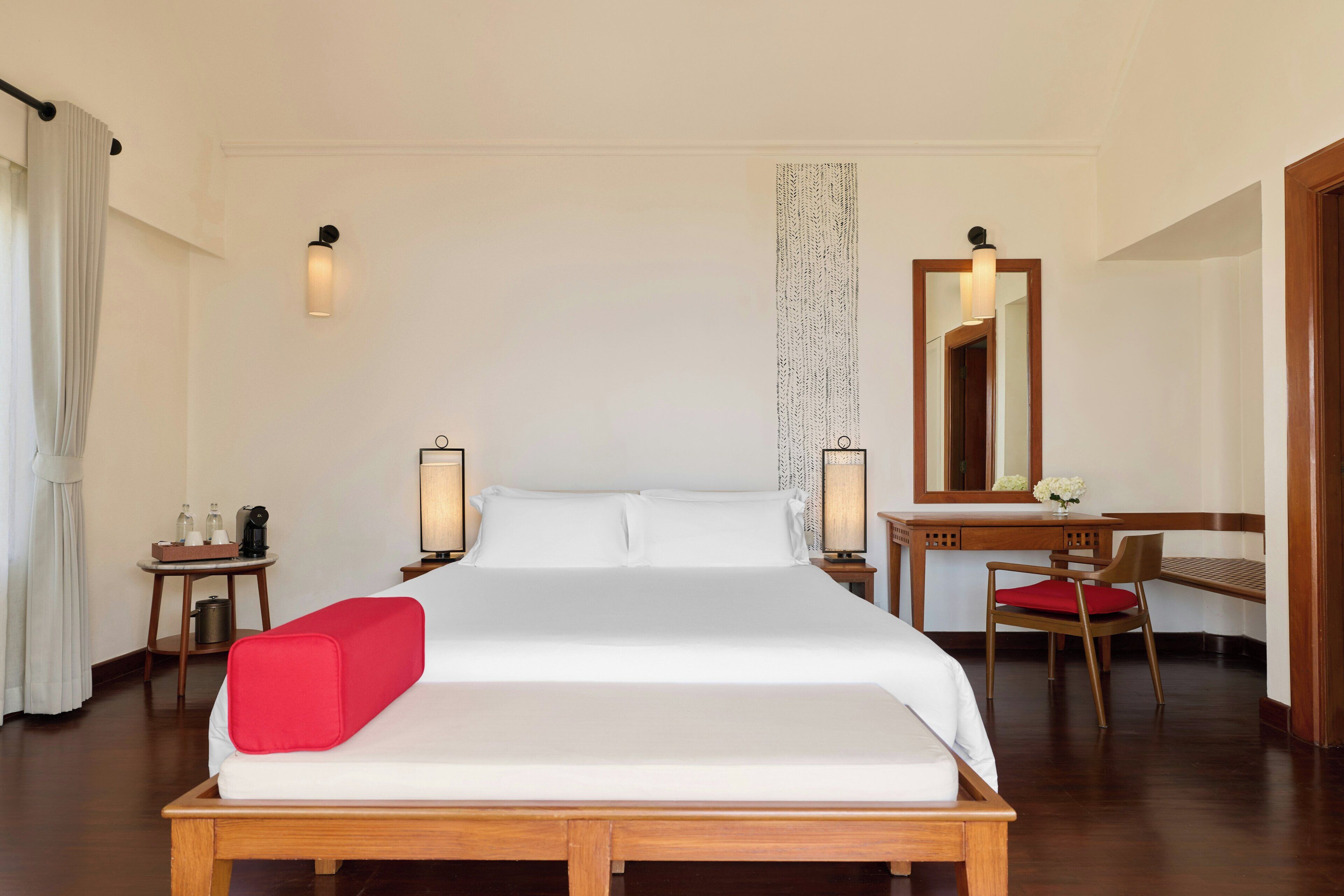 A hotel room with a bed, bedside tables, a desk, a chair, a mirror, and a curtain.