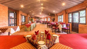 A spacious dining area with brick walls, large windows, and a high ceiling. Tables are set with red napkins and silverware.