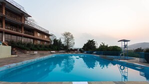 A swimming pool with a wooden deck, a lifeguard tower, and a building with balconies.