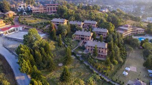 An aerial view of a residential area with multiple two-story houses, surrounded by greenery and a swimming pool.