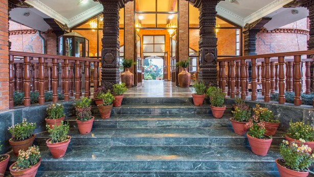 A grand staircase with ornate columns and potted plants, leading to a bright interior space.