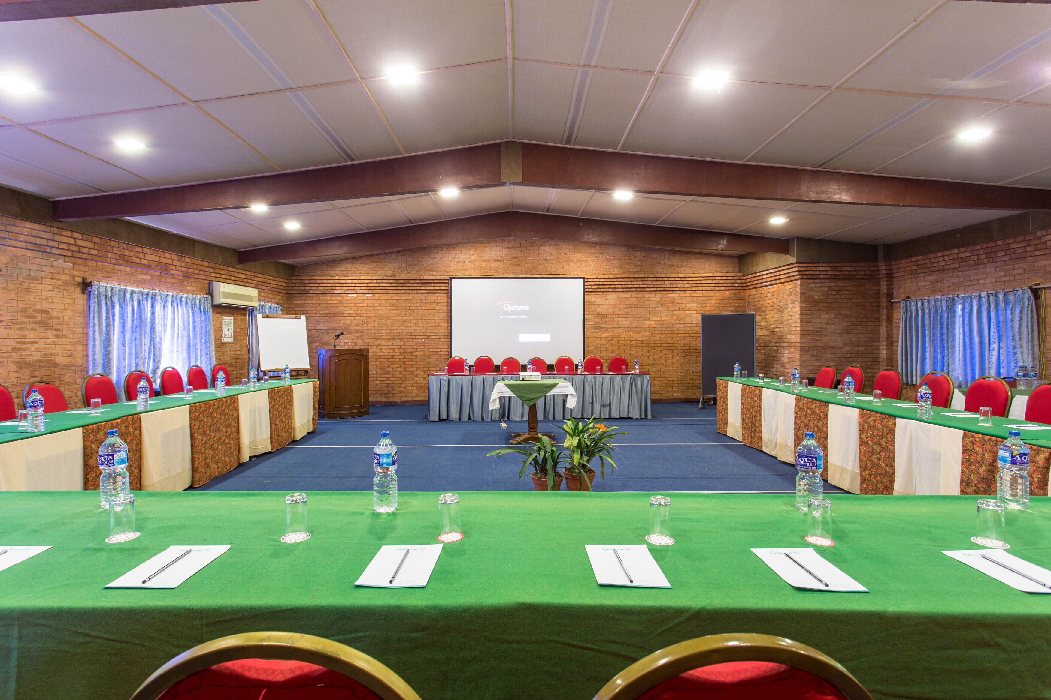 A conference room with a long table, red chairs, and a projector screen.