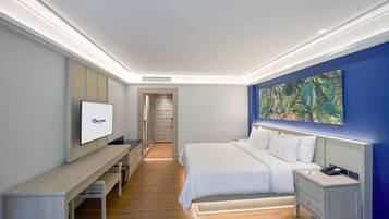 A modern hotel room with a large bed, a desk, a television, and a painting on the wall.