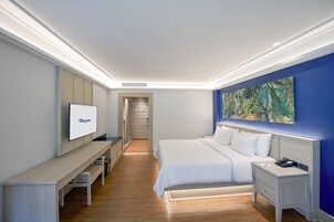 A modern hotel room with a large bed, a desk, a television, and a painting on the wall.