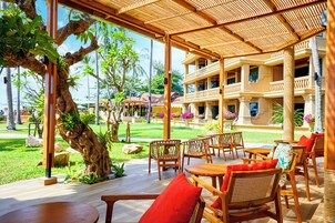 A covered outdoor seating area with wooden furniture and a view of a building with balconies.
