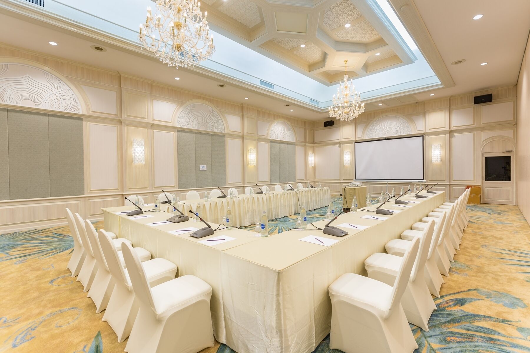 A conference room with a long table, chairs, microphones, and a projector screen.
