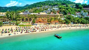 A beach with numerous colorful umbrellas and a boat in the water. - Beyond Kata (Karon)