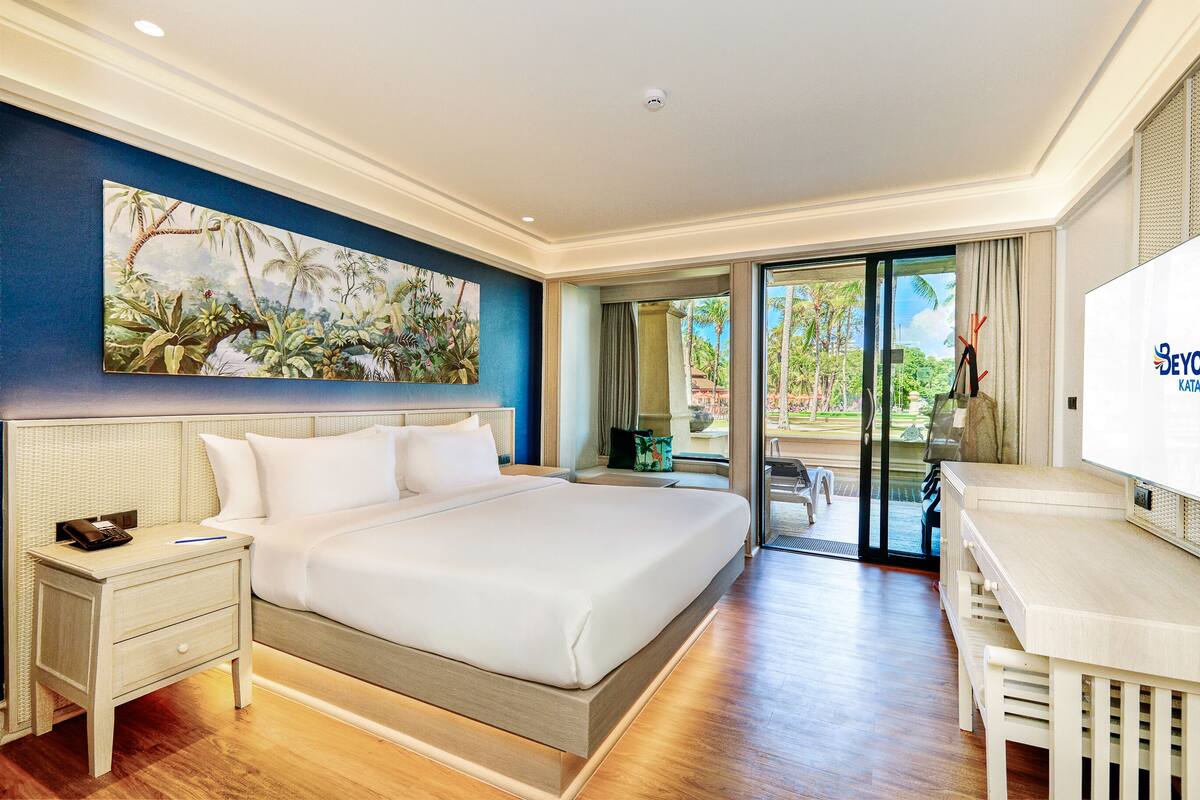 Une chambre d’hôtel avec un grand lit, un bureau, un tableau au mur et une vue sur l’extérieur.