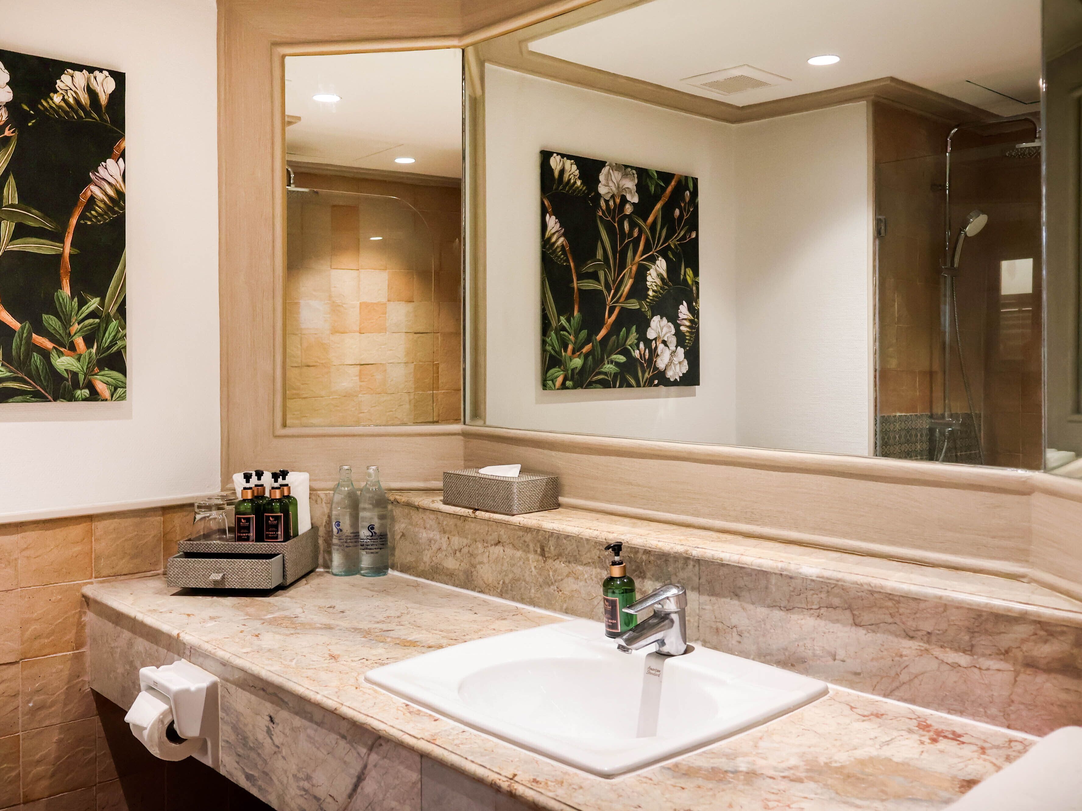 A bathroom with a marble sink, a large mirror, and two floral wall art pieces.