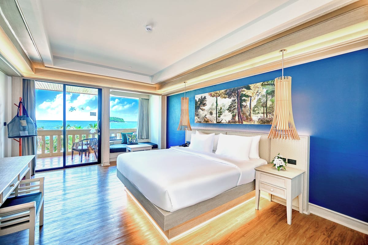 Une chambre d’hôtel avec un grand lit, un bureau et une vue sur l’océan depuis les portes du balcon.