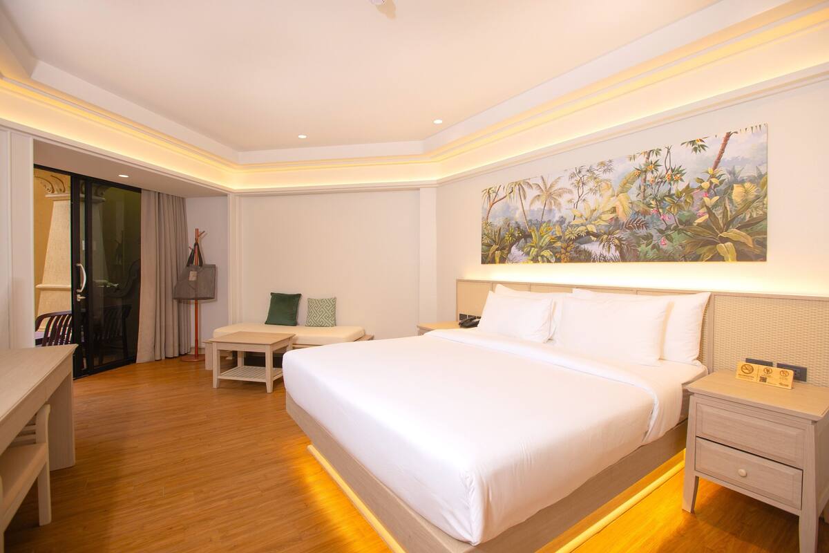 Une chambre d’hôtel avec un grand lit, des tables de chevet, un bureau et un tableau au mur.