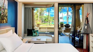 A hotel room with a bed, a sofa, a small table, and a view of the ocean through a glass door. - Beyond Kata (Karon)