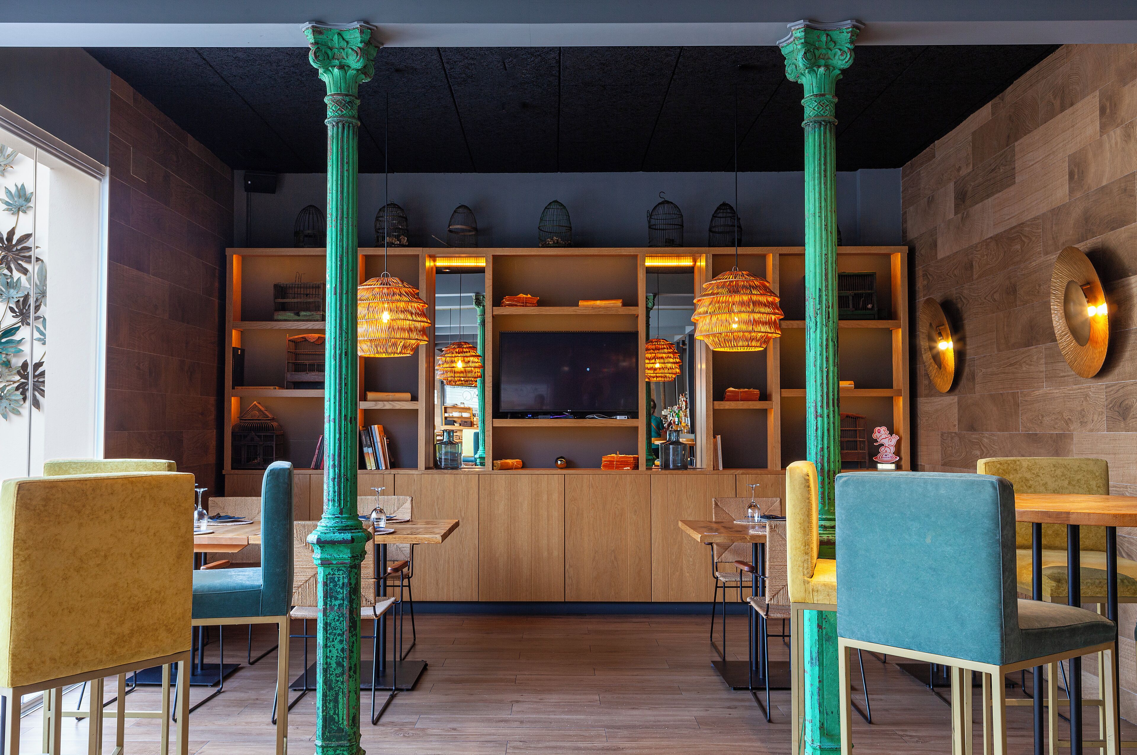 L’intérieur d’un restaurant avec des lambris en bois, des colonnes vertes et de nombreux luminaires suspendus.