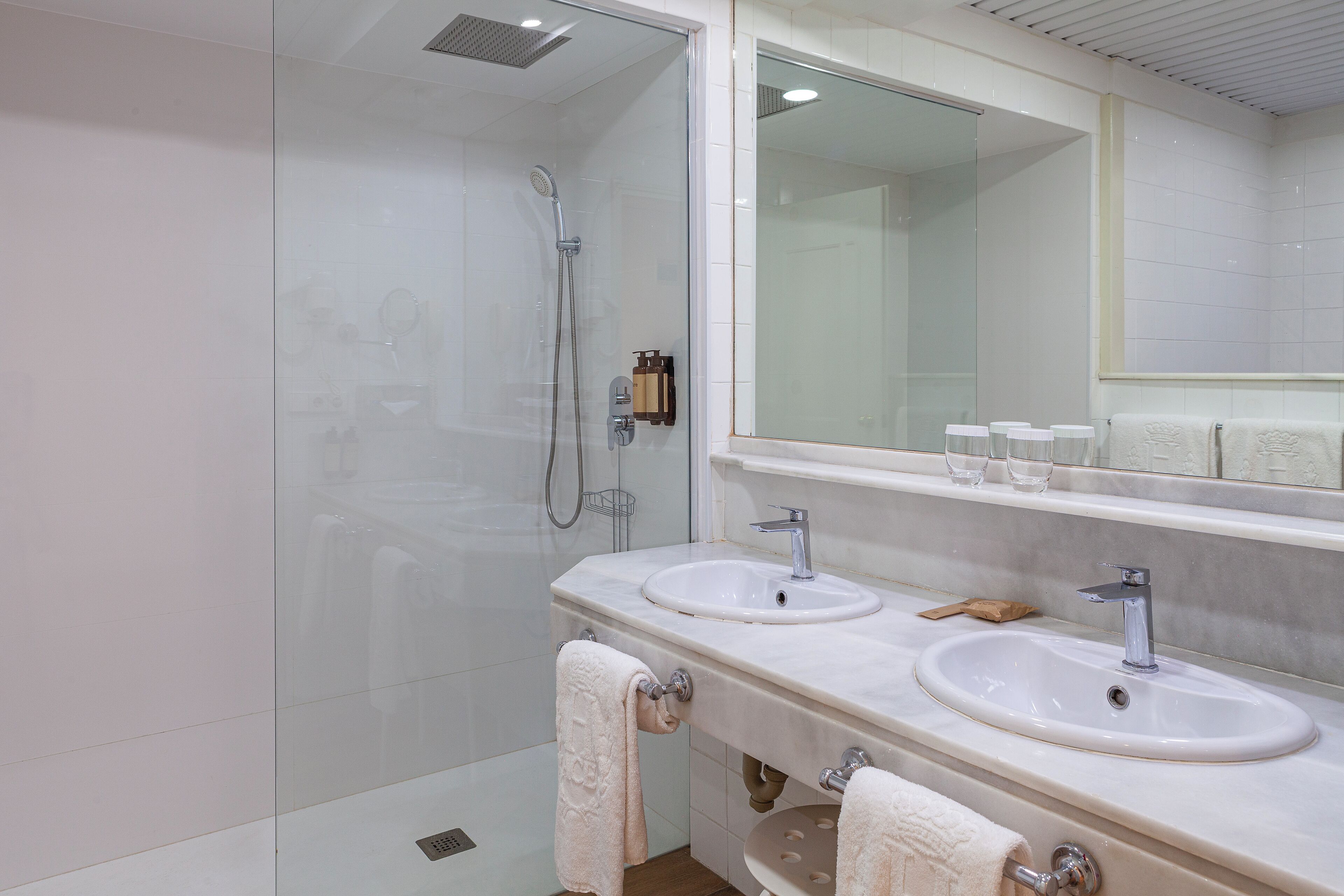 Un baño moderno con cabina de ducha de vidrio, dos lavamanos y un espejo grande.