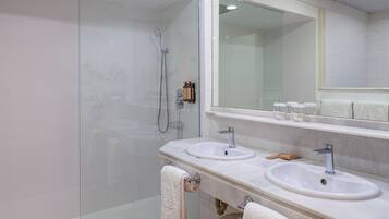 Un baño moderno con cabina de ducha de vidrio, dos lavamanos y un espejo grande.