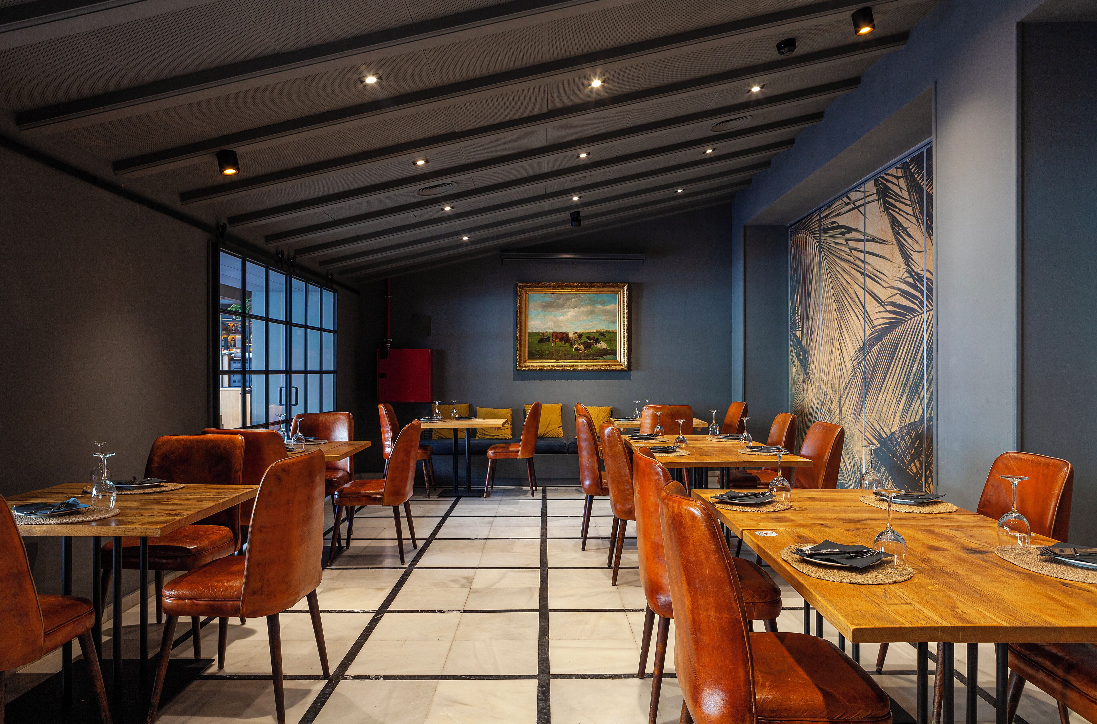 Un restaurant avec des tables en bois et des chaises orange, une grande peinture au mur et une vue dégagée sur l’extérieur grâce à de grandes fenêtres.