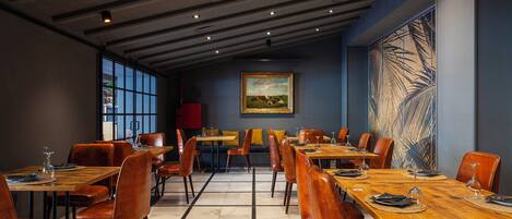 Un restaurant avec des tables en bois et des chaises orange, une grande peinture au mur et une vue dégagée sur l’extérieur grâce à de grandes fenêtres.