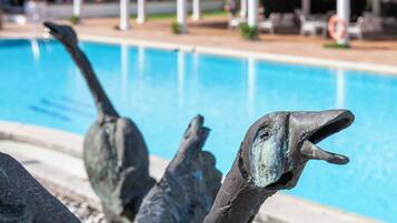 A pool area with a dolphin sculpture and lounge chairs.