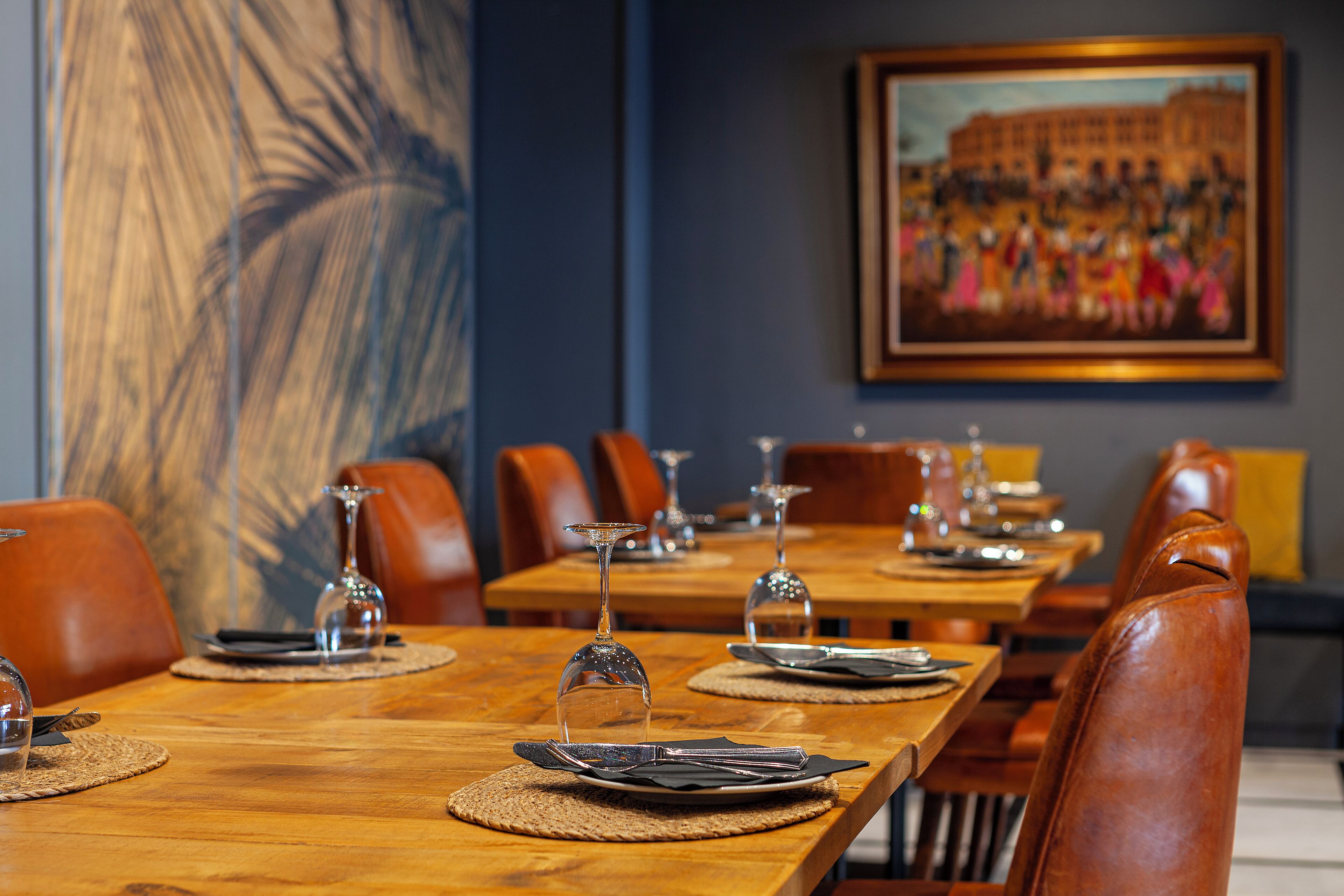 A dining area with wooden tables, leather chairs, and a large abstract painting on the wall.