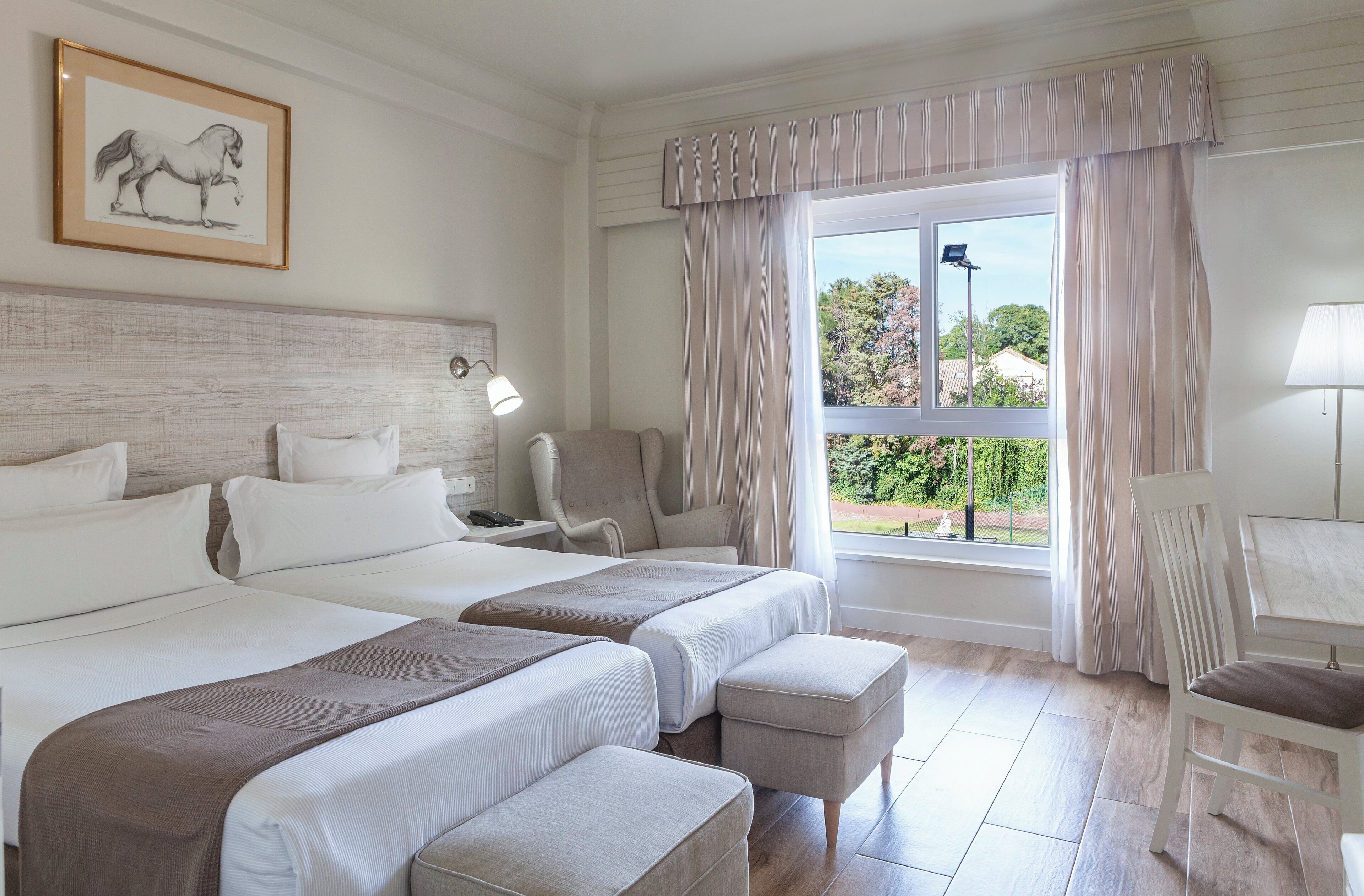 Habitación de hotel con dos camas, un escritorio, una silla y una ventana con cortinas.