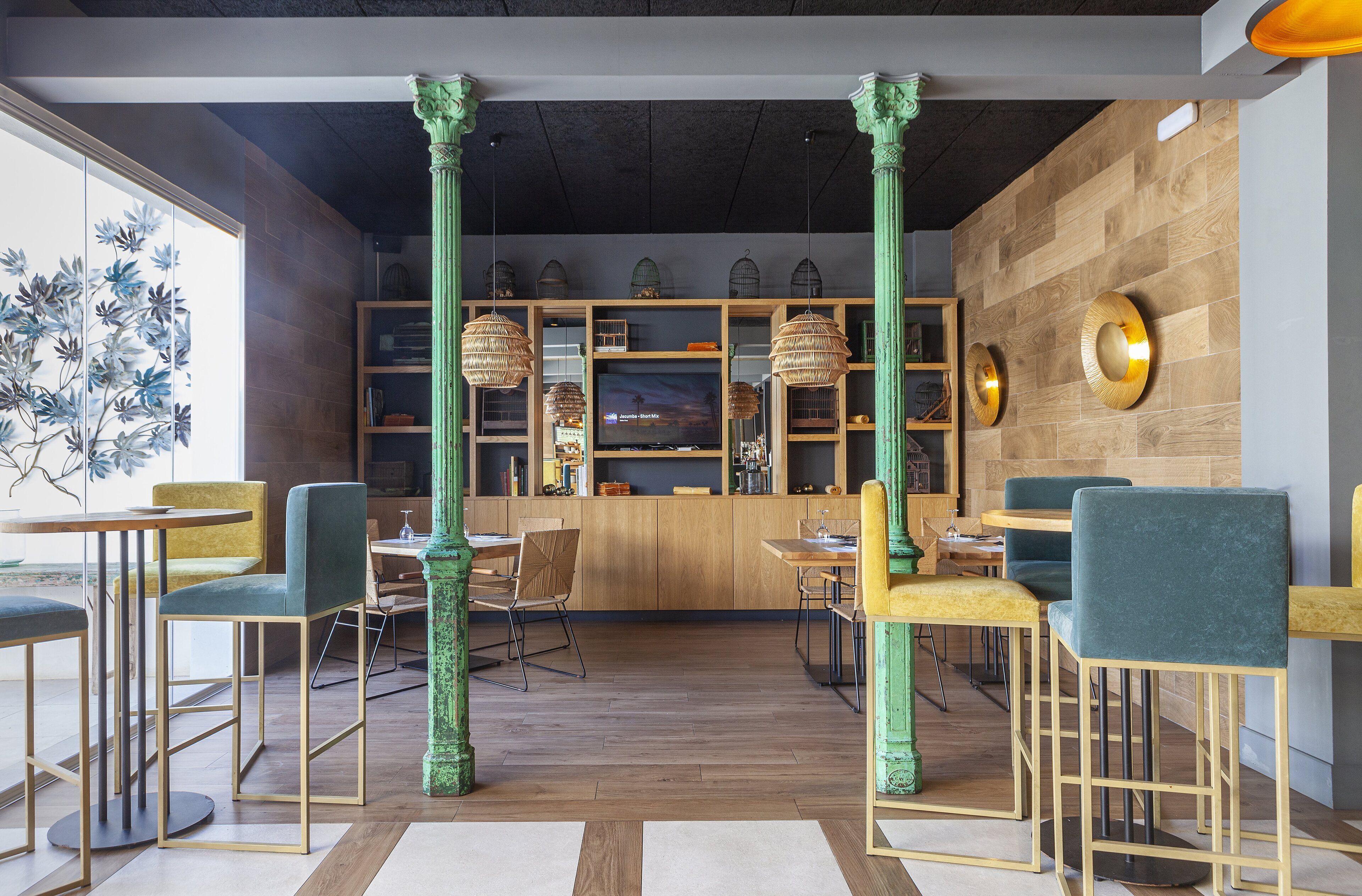 Un interior moderno con suelo de madera, columnas verdes y una zona de bar con asientos.