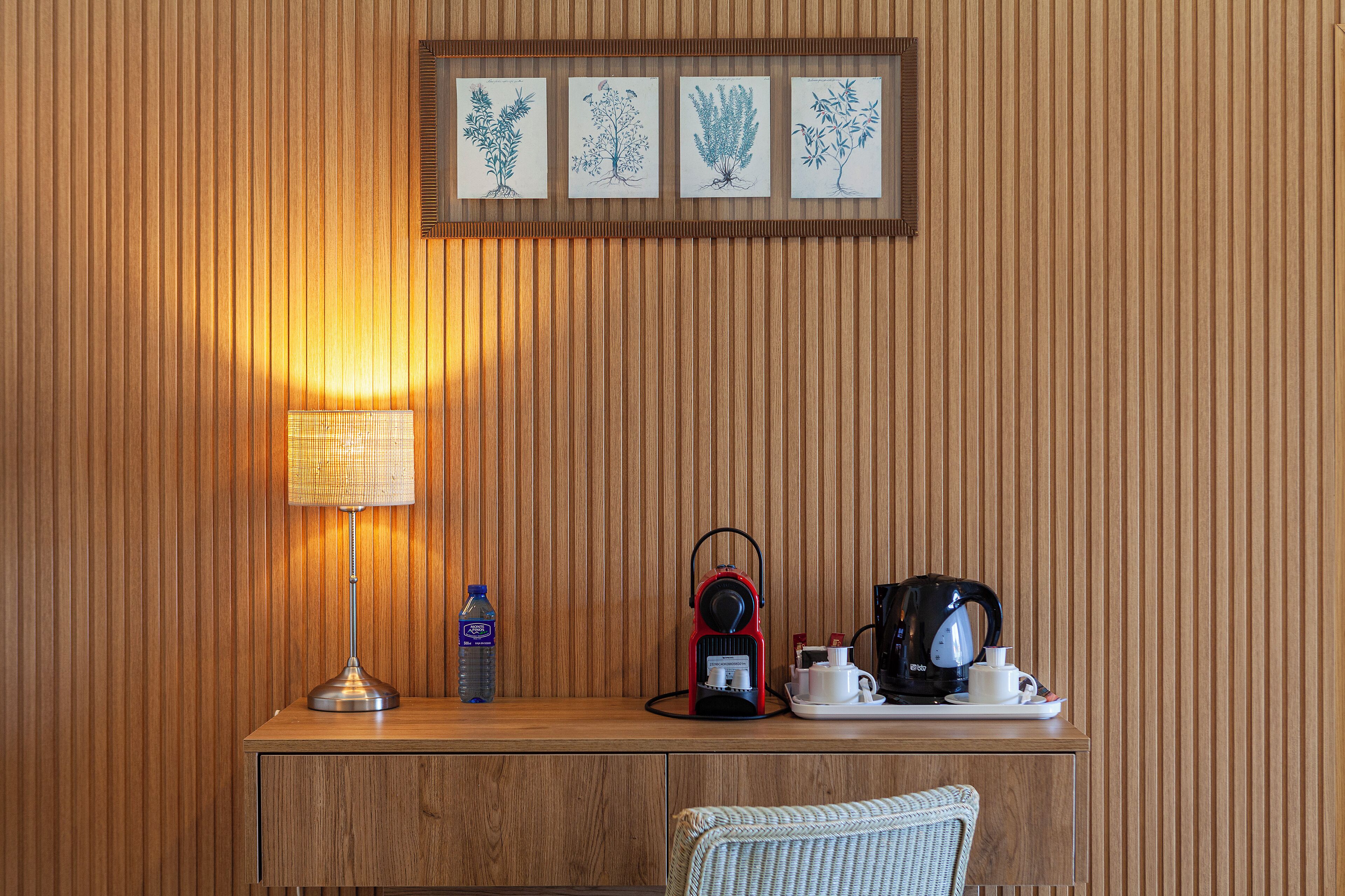 A wooden desk with a lamp, a water bottle, a red electric kettle, and a coffee maker.