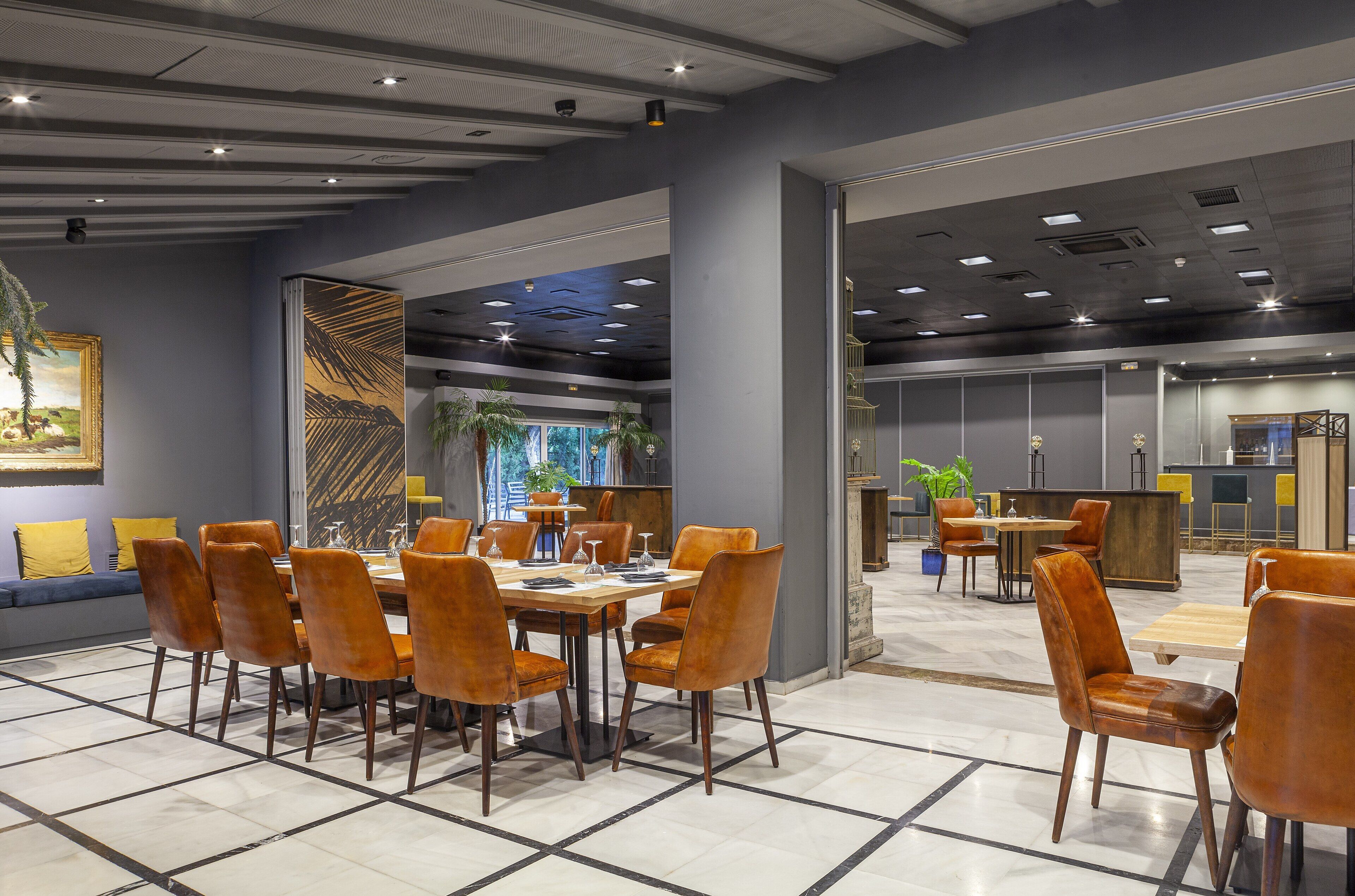 Ein moderner Essbereich mit einem langen Tisch und Stühlen, eine Bar mit Hockern sowie eine Sitzecke mit einer Couch und Sesseln.