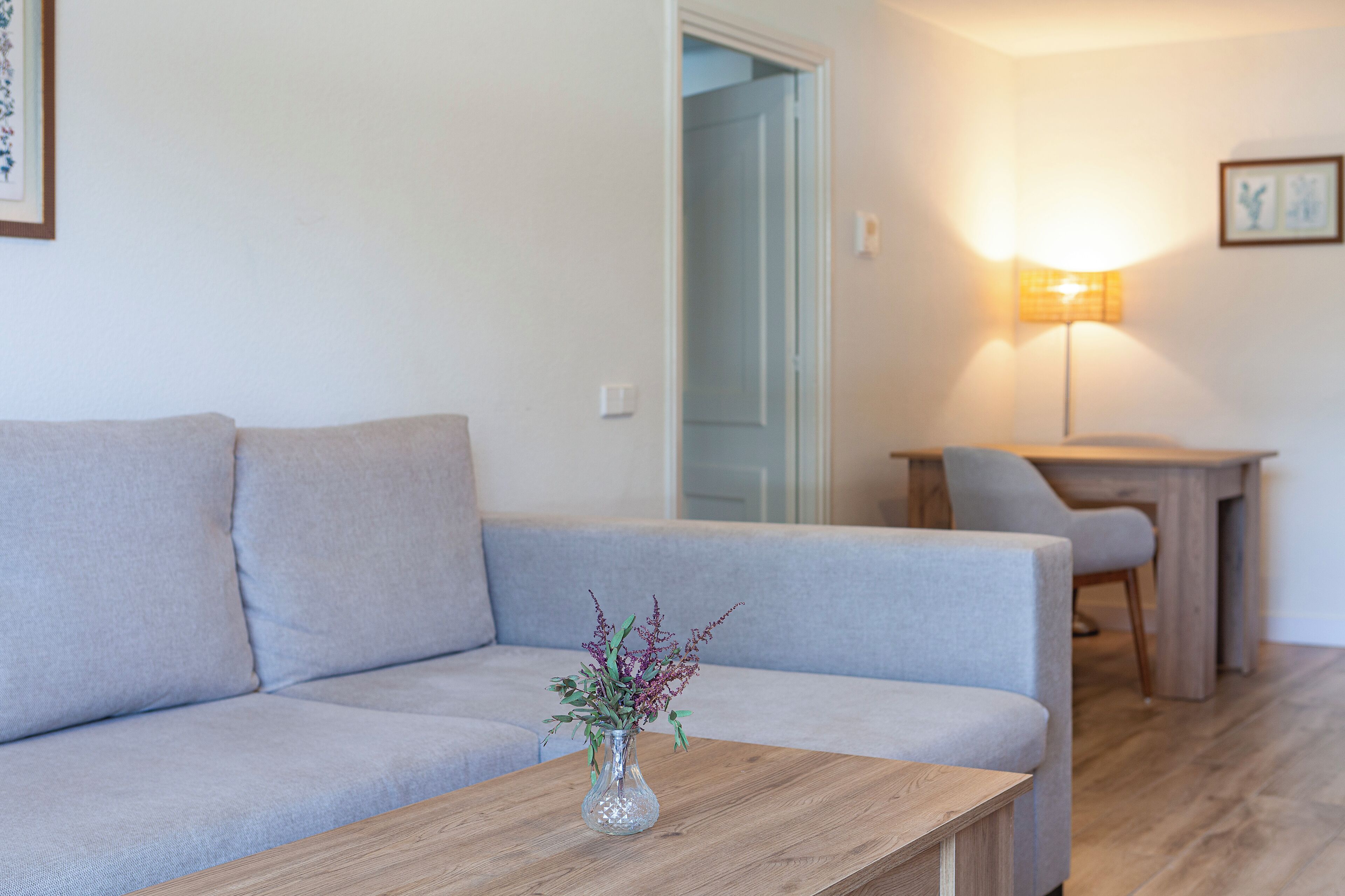 A living room with a grey sofa, a wooden coffee table, and a vase with flowers.