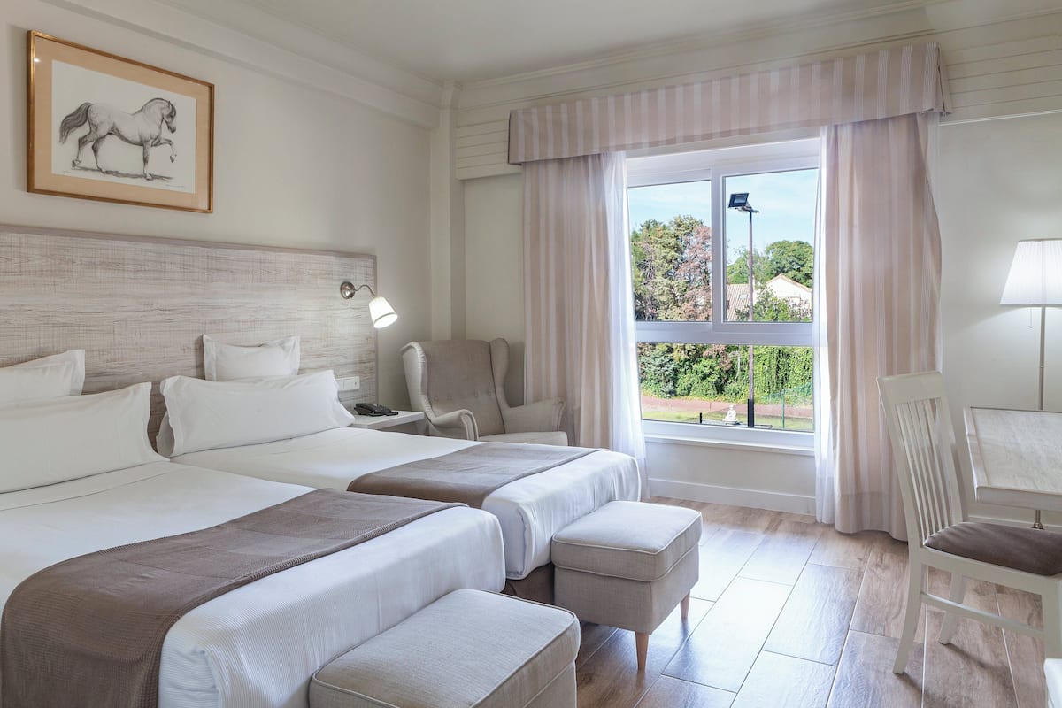 Habitación de hotel con dos camas, un escritorio, una silla y una ventana con cortinas.