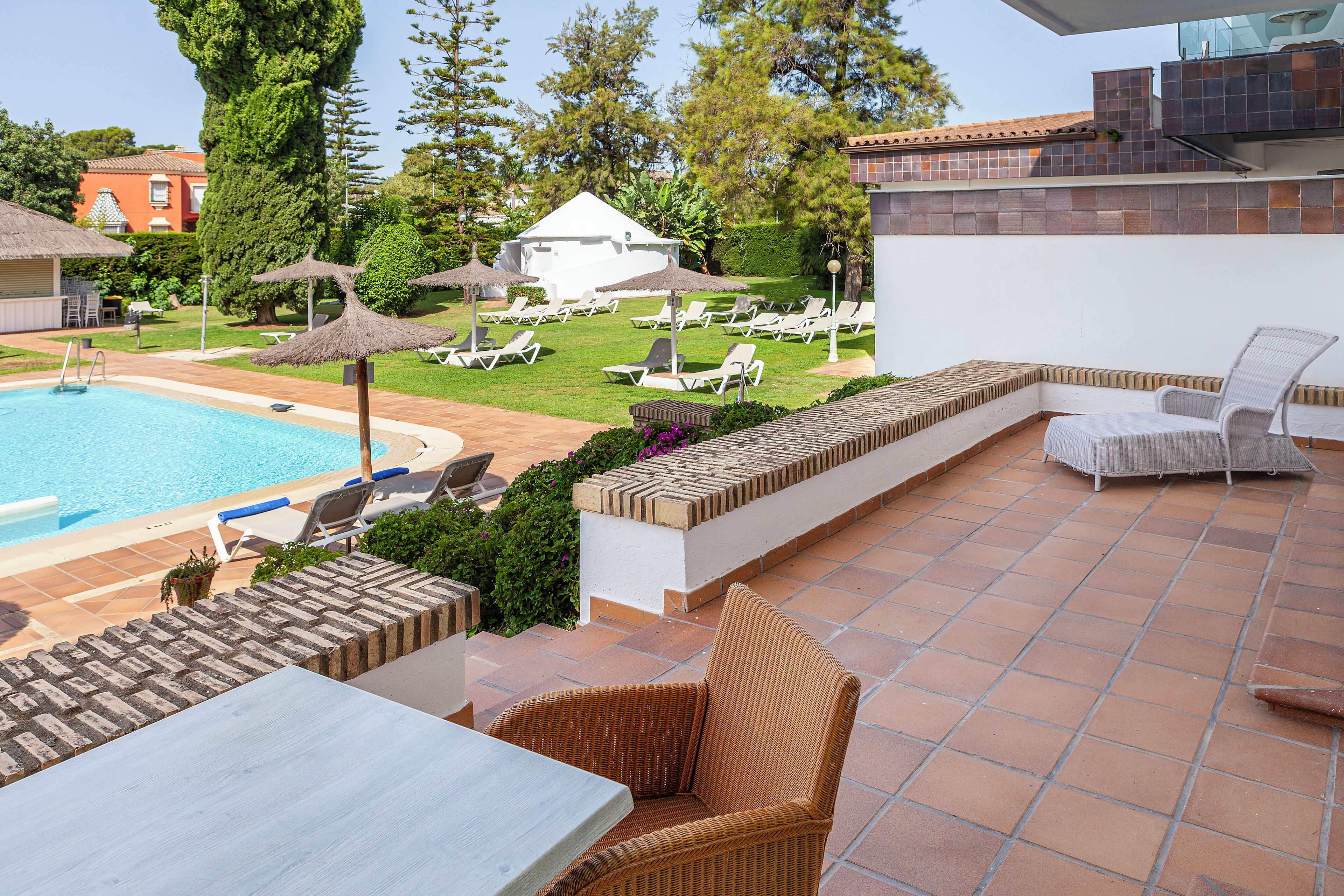 Ein Poolbereich mit Liegestühlen, einem Tisch und Blick auf Pool und Garten.