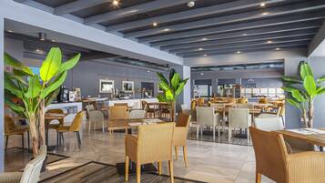 A spacious indoor area with multiple seating arrangements, a kitchen area, and large windows.