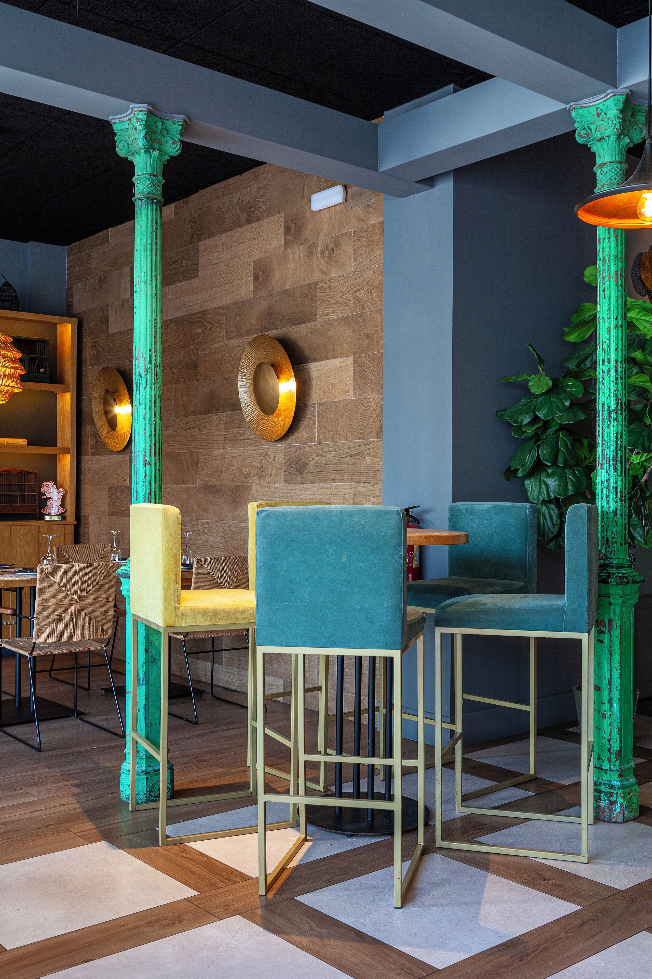 Un comedor con columnas verdes, suelo de madera y sillas azules.
