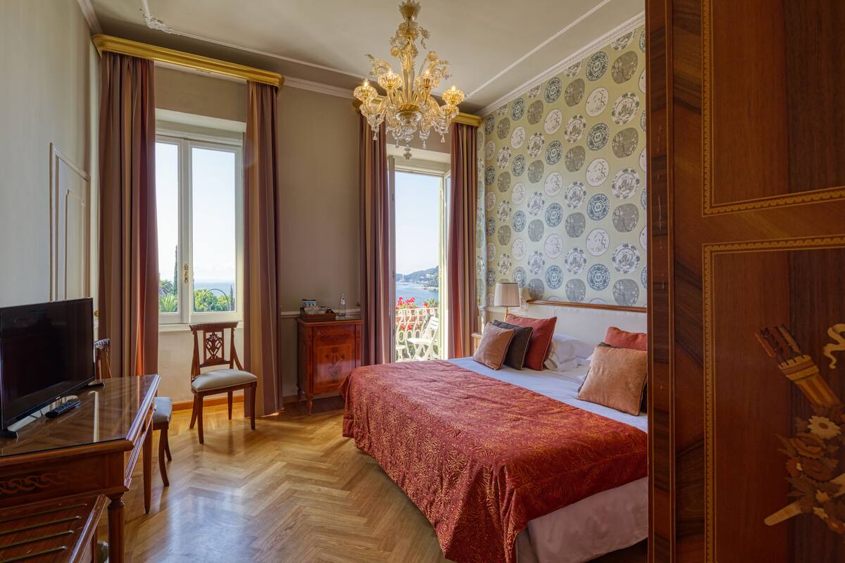 A bedroom with a large bed, a TV, a wooden dresser, and a view of the outdoors.