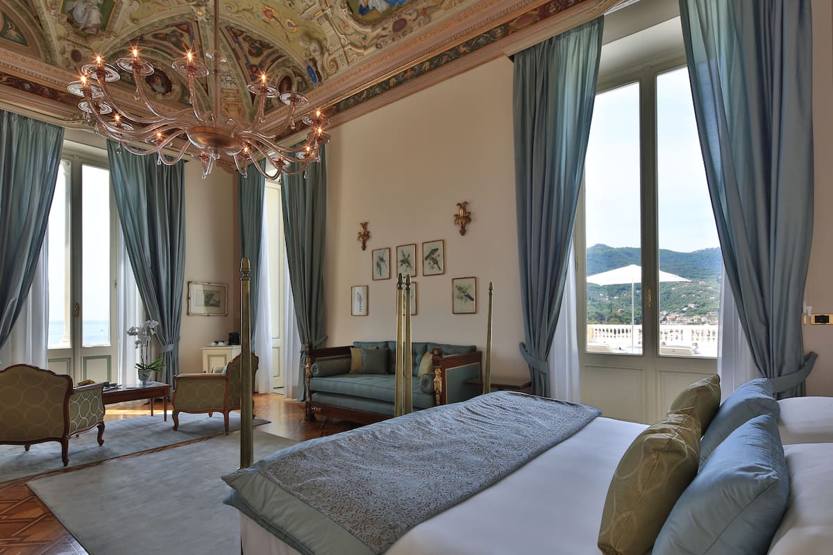 A spacious room with a large bed, a chandelier, and a view of the mountains through the window.