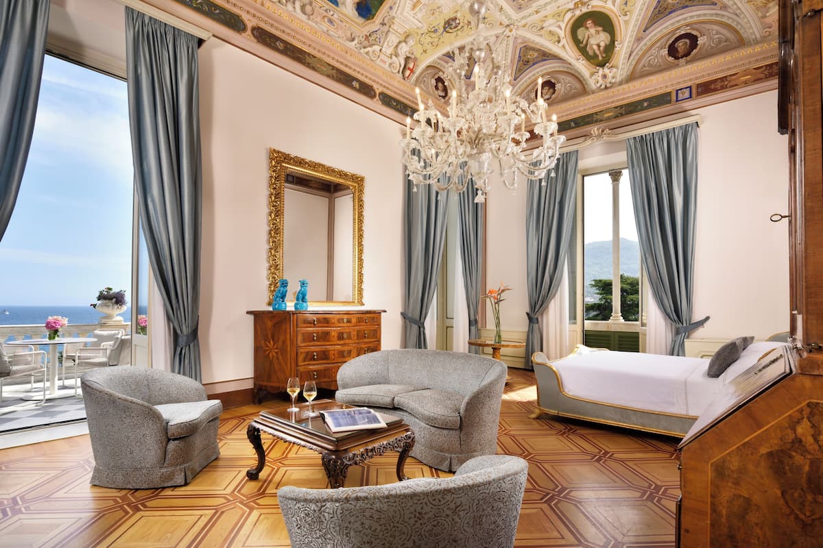 A luxurious bedroom with a large bed, two armchairs, a wooden dresser, and a chandelier.